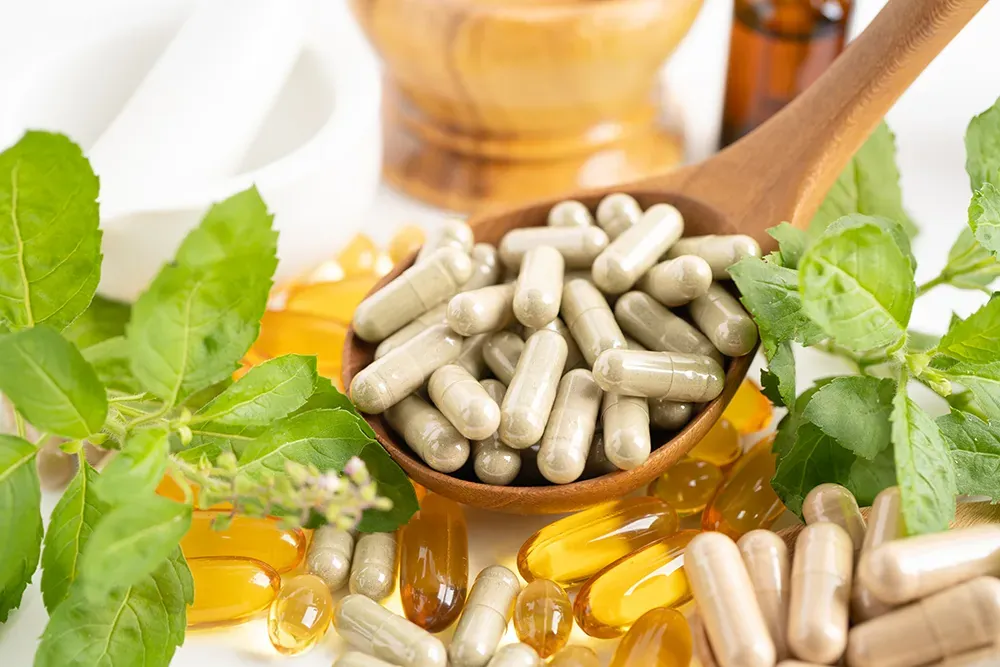 Capsules on a wooden spoon with fresh herbs